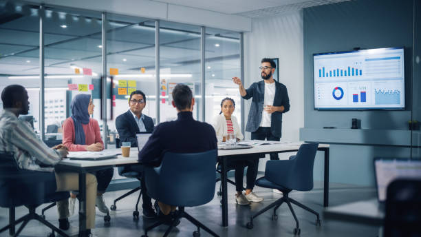 diverse modern office: businessman leads business meeting with managers, talks, uses presentation tv with statistics, infographics. digital entrepreneurs work on e-commerce project. - 会议 個照片及圖片檔